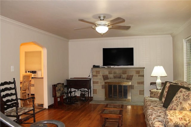 living room featuring arched walkways, a ceiling fan, ornamental molding, wood finished floors, and a fireplace