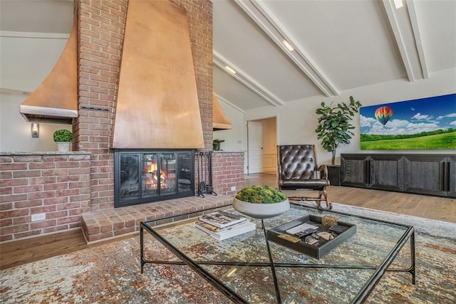 living room with hardwood / wood-style floors, high vaulted ceiling, a brick fireplace, beam ceiling, and brick wall