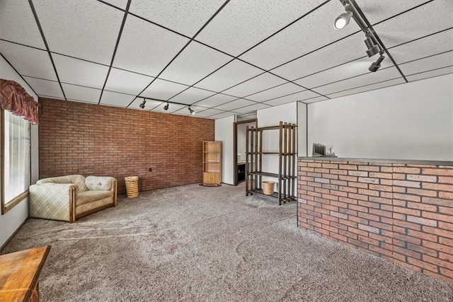 interior space with rail lighting, carpet flooring, a paneled ceiling, and brick wall