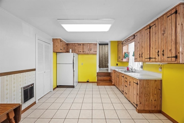 kitchen featuring white refrigerator, light tile patterned floors, sink, a fireplace, and crown molding