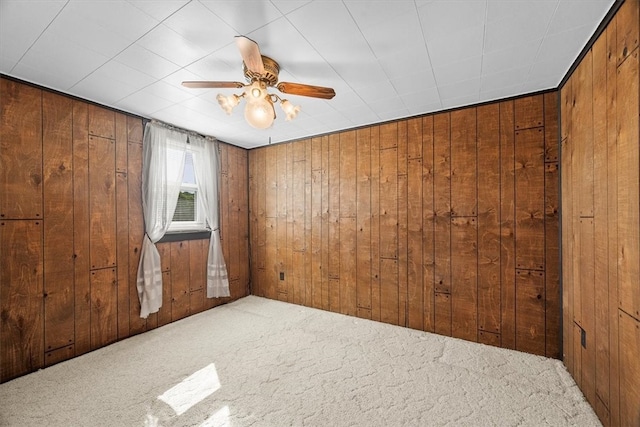 unfurnished room featuring carpet, wood walls, and ceiling fan