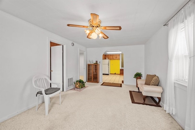 sitting room featuring ceiling fan, ornamental molding, and light carpet