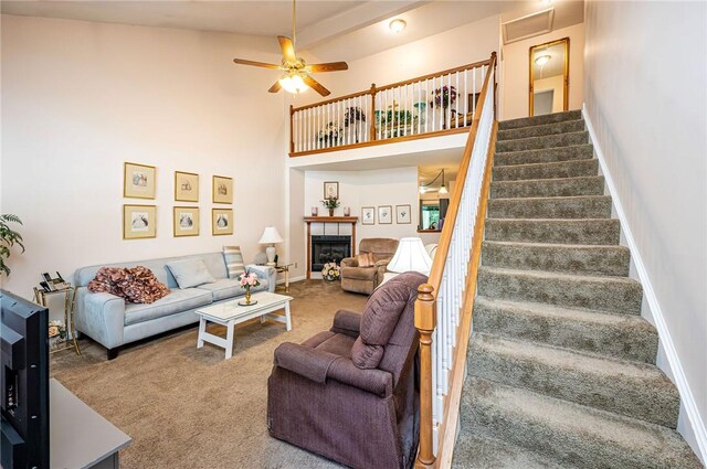 carpeted living room featuring high vaulted ceiling, ceiling fan, beamed ceiling, and a tiled fireplace