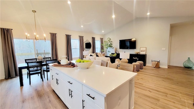 kitchen with pendant lighting, white cabinets, vaulted ceiling, light wood-type flooring, and a kitchen island