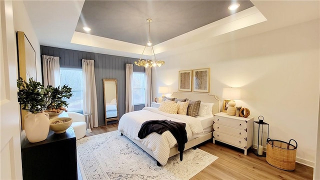 bedroom featuring a raised ceiling, light hardwood / wood-style floors, and a notable chandelier