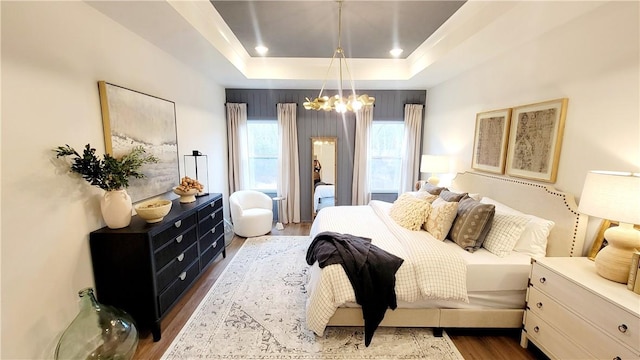 bedroom with hardwood / wood-style floors, an inviting chandelier, and a tray ceiling