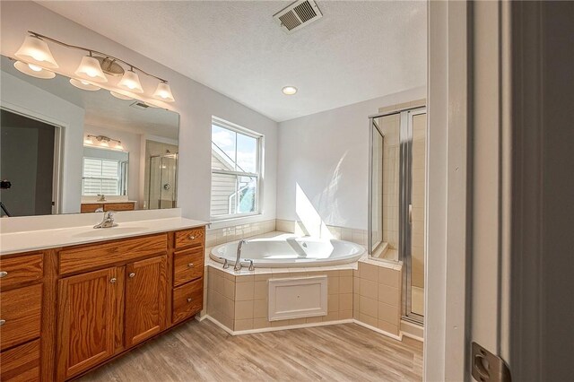 bathroom with a textured ceiling, hardwood / wood-style flooring, shower with separate bathtub, and vanity