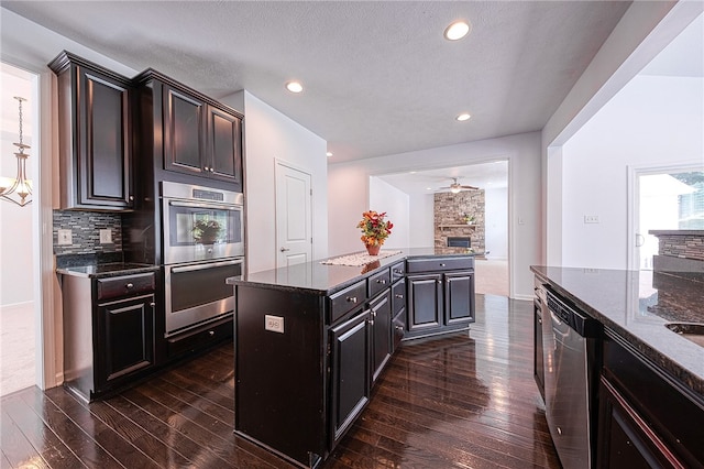 kitchen featuring appliances with stainless steel finishes, dark hardwood / wood-style floors, dark stone counters, a center island, and ceiling fan