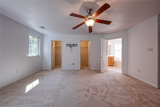 unfurnished bedroom with light colored carpet, a spacious closet, a closet, ceiling fan, and connected bathroom