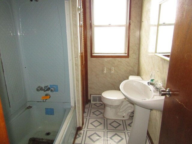 bathroom with bathing tub / shower combination, toilet, a healthy amount of sunlight, and tile patterned floors