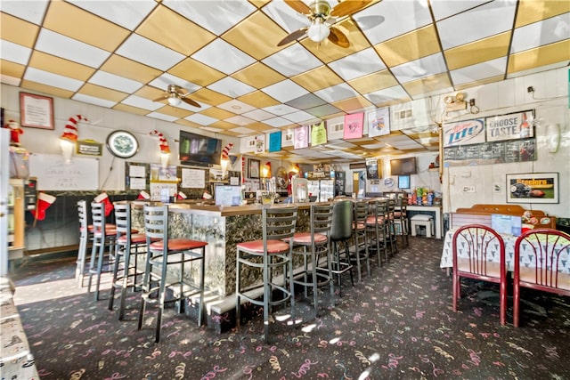 interior space with ceiling fan, carpet, bar area, and a paneled ceiling