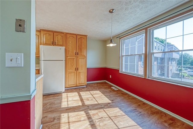 kitchen featuring a textured ceiling, white refrigerator, light wood-type flooring, and decorative light fixtures