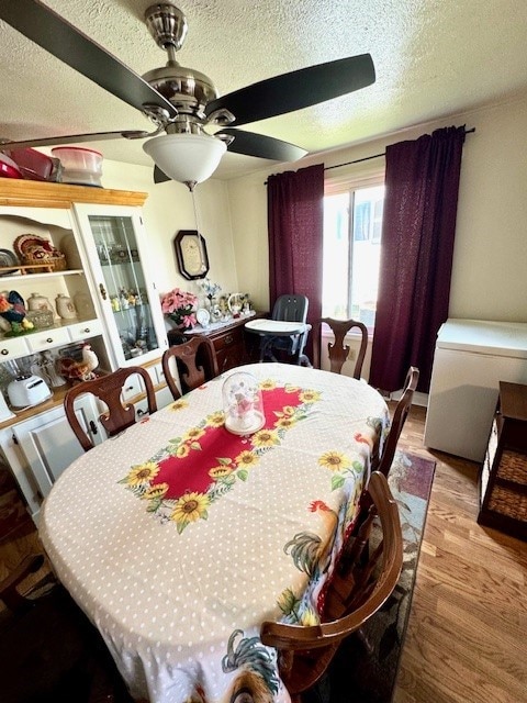 dining area with ceiling fan, hardwood / wood-style flooring, and a textured ceiling