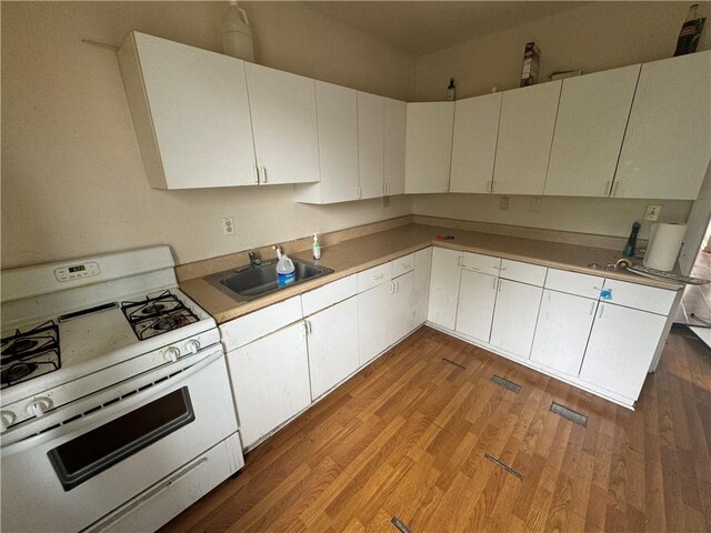 175 Penn Ave, Mount Oliver, PA 15210 - kitchen with light countertops, gas range gas stove, a sink, white cabinets, and wood finished floors