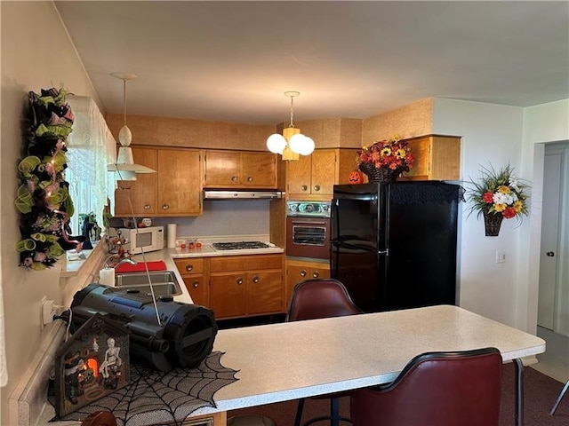 kitchen featuring stainless steel gas cooktop, oven, sink, black refrigerator, and kitchen peninsula