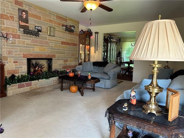 carpeted living room with ceiling fan and a stone fireplace