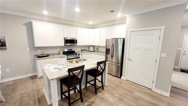 kitchen with a kitchen bar, light stone counters, light hardwood / wood-style floors, a kitchen island with sink, and stainless steel appliances