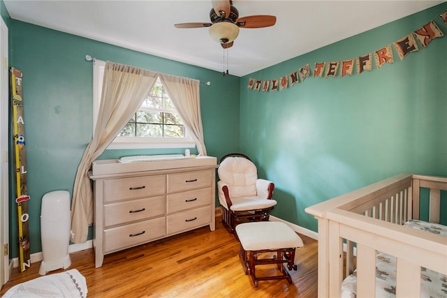 bedroom featuring ceiling fan, a crib, and light hardwood / wood-style floors