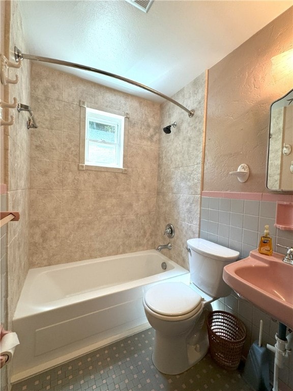 full bathroom featuring tiled shower / bath, decorative backsplash, tile patterned floors, tile walls, and toilet