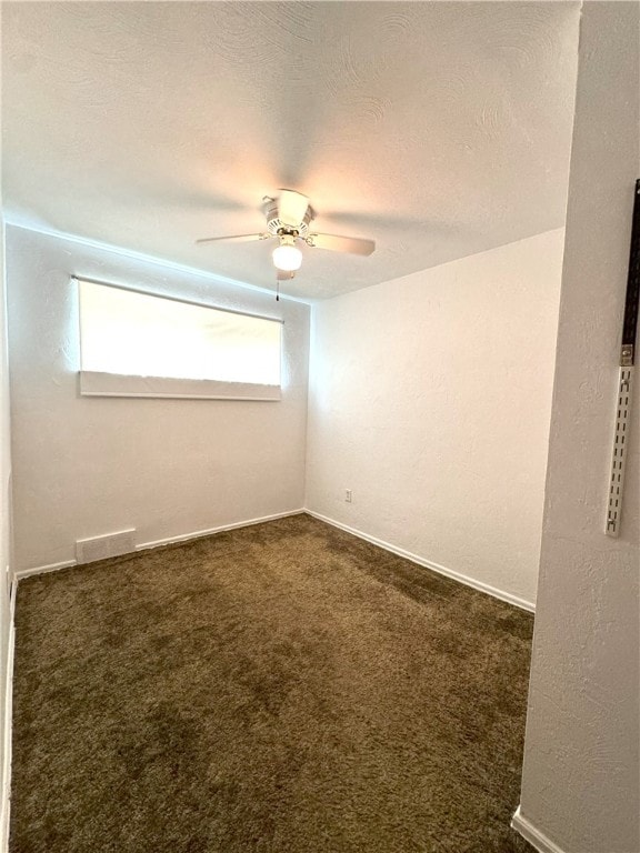 spare room featuring ceiling fan, dark colored carpet, and a textured ceiling