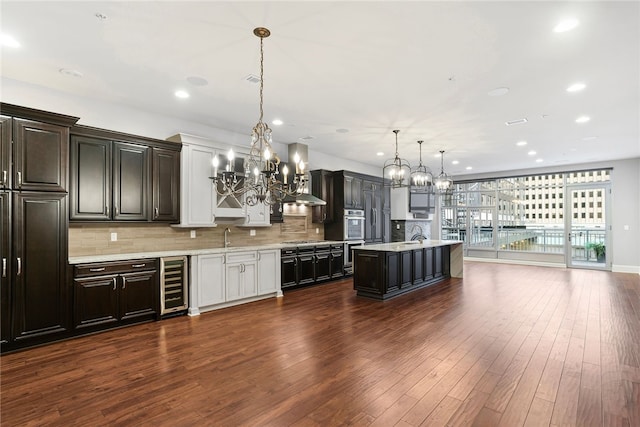 kitchen featuring dark hardwood / wood-style flooring, decorative light fixtures, beverage cooler, and a kitchen island with sink