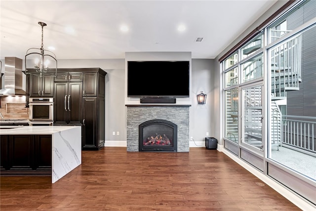 living room featuring a stone fireplace, a chandelier, and dark hardwood / wood-style floors