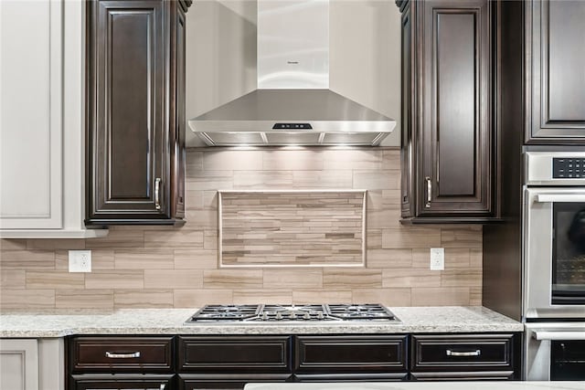 kitchen featuring wall chimney exhaust hood, dark brown cabinetry, backsplash, and appliances with stainless steel finishes