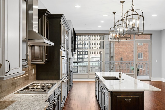 kitchen featuring sink, wall chimney exhaust hood, dark hardwood / wood-style flooring, decorative light fixtures, and a kitchen island with sink