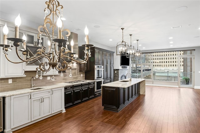 kitchen with tasteful backsplash, stainless steel appliances, a kitchen island with sink, dark wood-type flooring, and hanging light fixtures