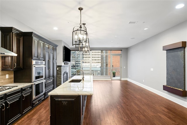 kitchen with sink, dark hardwood / wood-style floors, a chandelier, a center island with sink, and appliances with stainless steel finishes