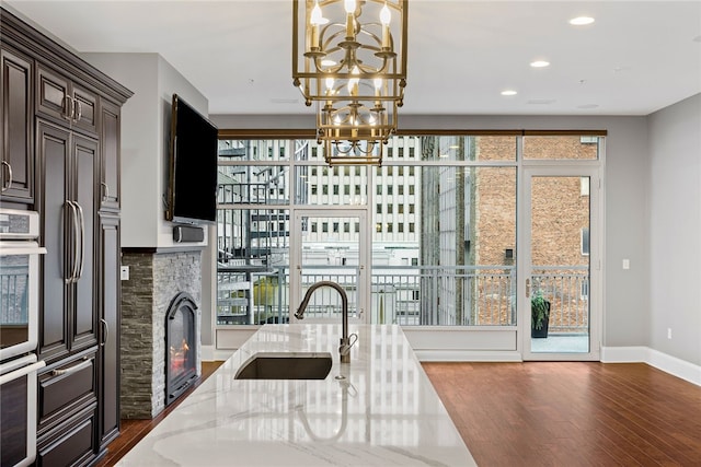 kitchen with light stone countertops, sink, an inviting chandelier, dark hardwood / wood-style flooring, and decorative light fixtures