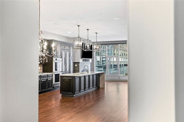 kitchen with backsplash, a center island with sink, dark wood-type flooring, and sink