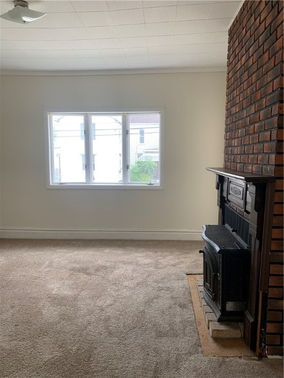 unfurnished living room featuring brick wall, ornamental molding, light colored carpet, and a wood stove