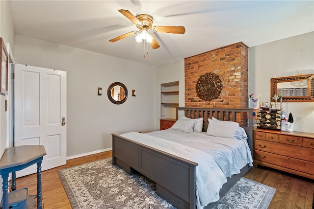 bedroom with hardwood / wood-style floors, ceiling fan, and brick wall