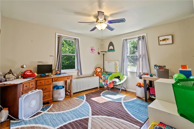 office space with a wealth of natural light, ceiling fan, radiator, and hardwood / wood-style floors