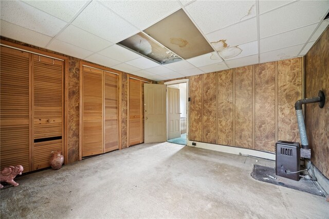 interior space featuring carpet flooring, wood walls, a wood stove, and a drop ceiling