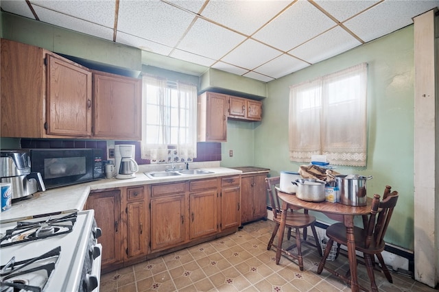 kitchen with sink, a drop ceiling, gas range gas stove, and light tile patterned floors