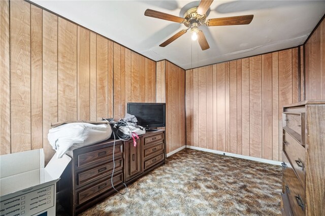 interior space featuring dark colored carpet, ceiling fan, and wood walls