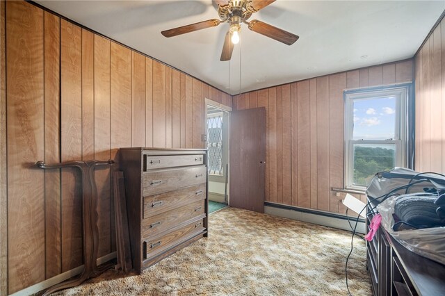 carpeted bedroom featuring multiple windows, wood walls, a baseboard radiator, and ceiling fan