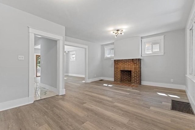 unfurnished living room with a brick fireplace, visible vents, baseboards, and wood finished floors