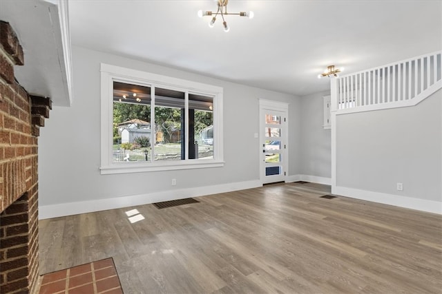 unfurnished living room featuring hardwood / wood-style flooring, an inviting chandelier, brick wall, and a fireplace