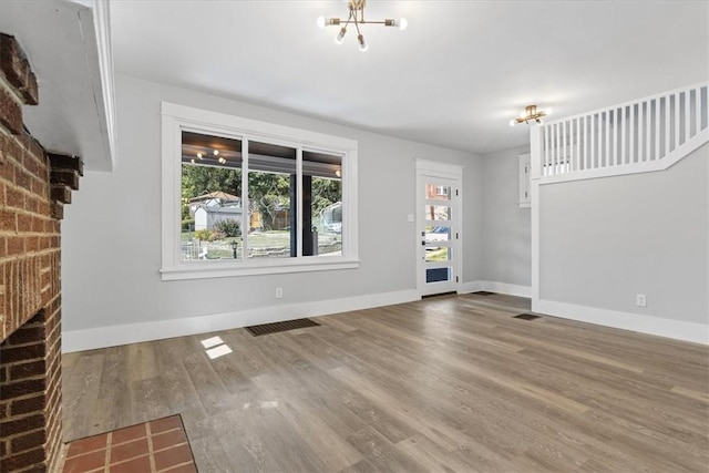 unfurnished living room with visible vents, a notable chandelier, baseboards, and wood finished floors