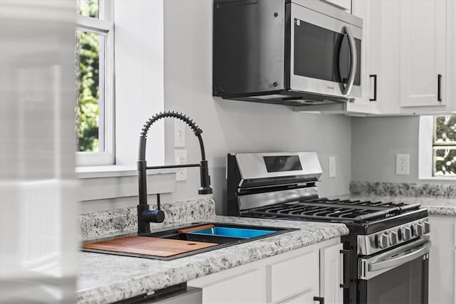 kitchen featuring appliances with stainless steel finishes, white cabinets, a sink, and light stone countertops