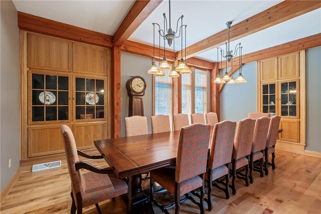 dining area featuring light wood-type flooring, beamed ceiling, and an inviting chandelier