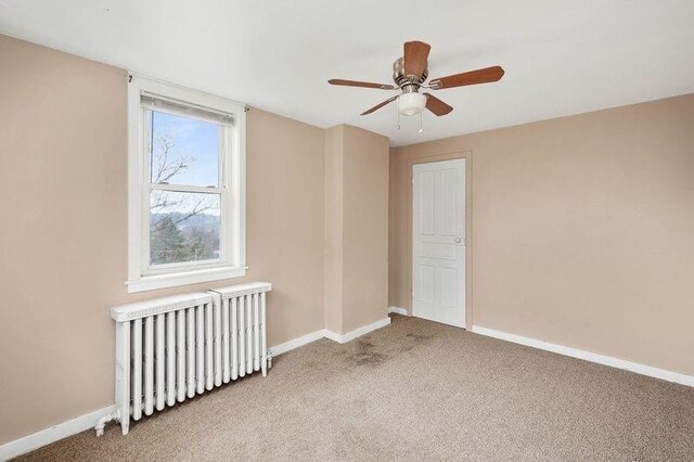 unfurnished bedroom with radiator heating unit, ceiling fan, and carpet