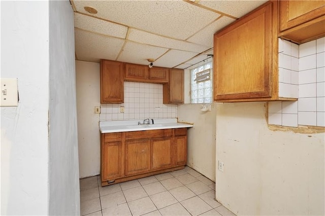 kitchen with sink, tasteful backsplash, light tile patterned floors, and a drop ceiling