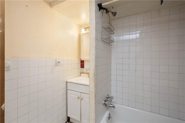 bathroom with tiled shower / bath combo, vanity, and tile walls