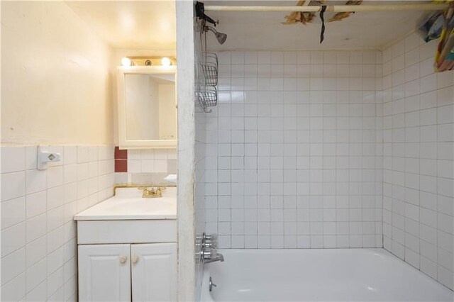 bathroom featuring tiled shower / bath combo, vanity, and tile walls