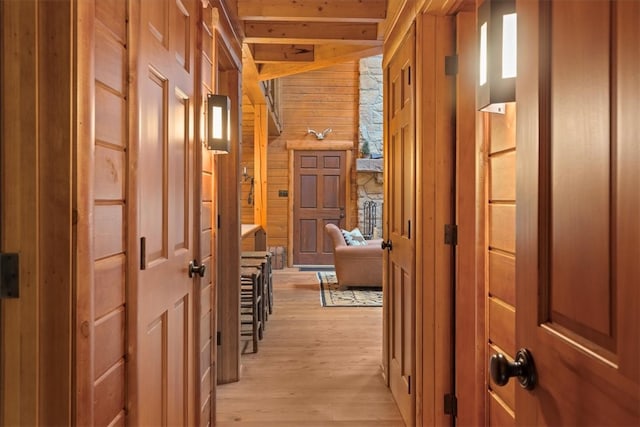 hall with light wood-type flooring, beamed ceiling, and wooden walls