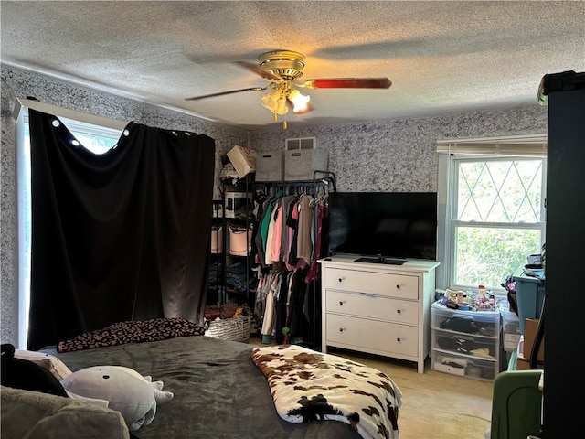 bedroom with wallpapered walls, ceiling fan, visible vents, and a textured ceiling